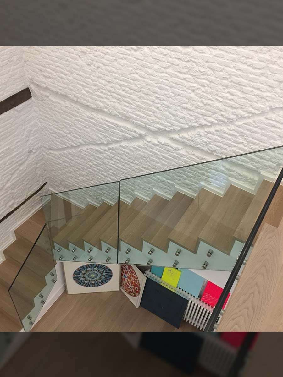 Escalera con escalones de madera, barandilla de cristal y techo blanco texturizado.