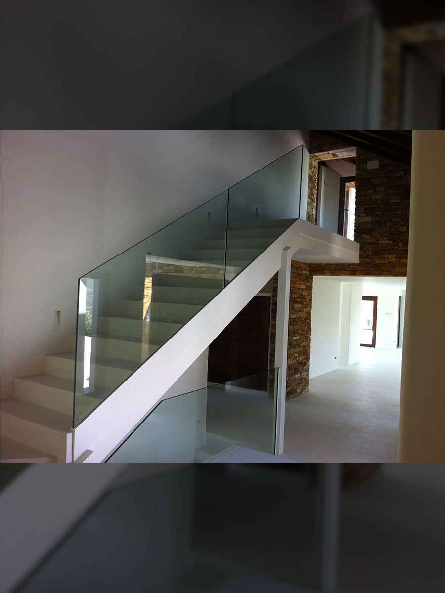 Escalera moderna con barandilla de cristal, escalones de madera y una gran planta en maceta en un espacio lleno de luz.