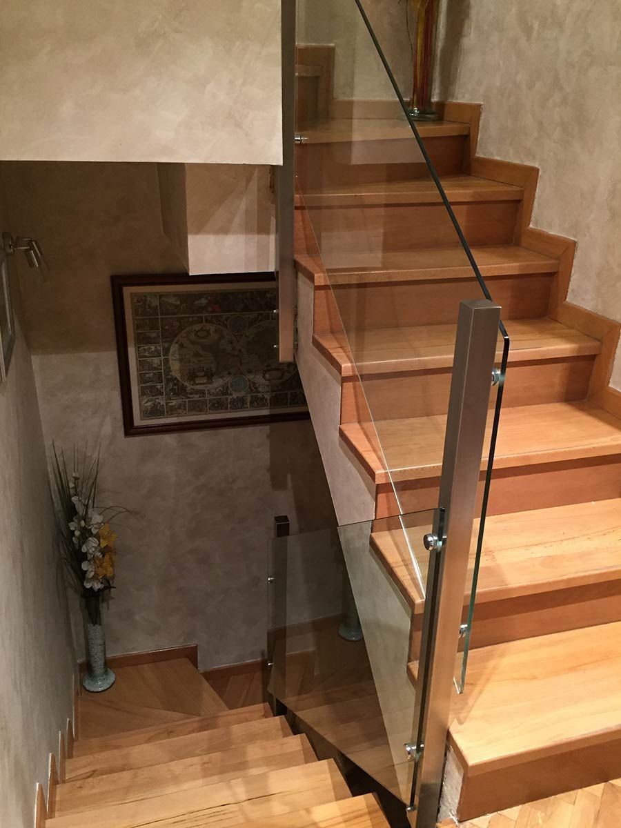 Escalera con barandilla de cristal, escalones y suelo de madera, paredes neutras, arte enmarcado.