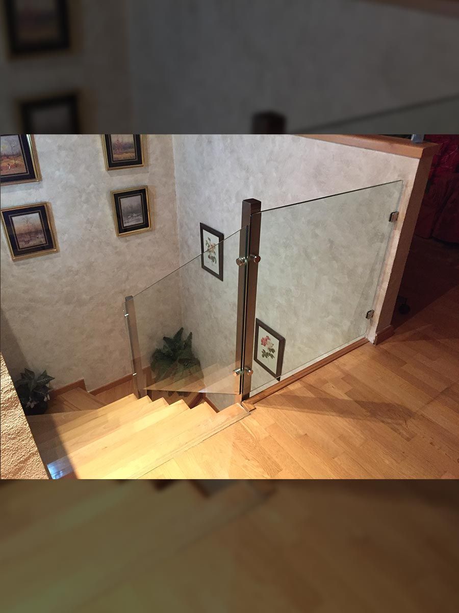 Escalera con barandilla de cristal, escalones y suelo de madera, paredes neutras, arte enmarcado.