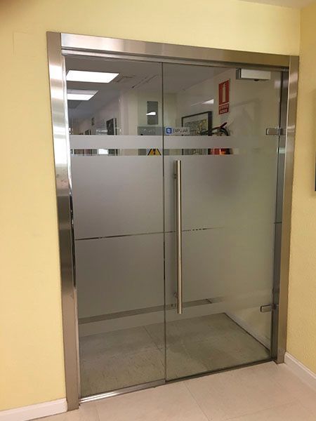 Puertas dobles de vidrio con vidrio esmerilado y marco de acero inoxidable en un edificio.