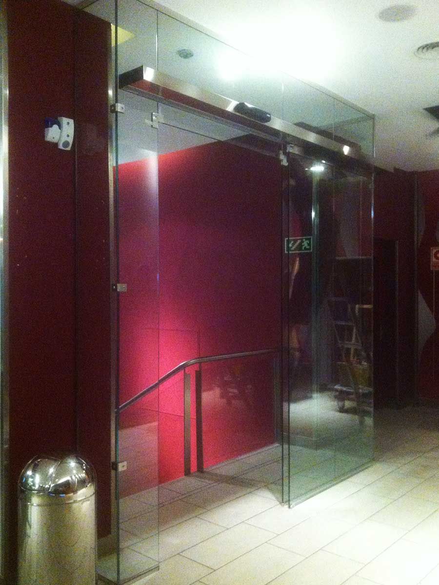 Puertas automáticas de cristal, paredes rojas y un cubo de basura de acero inoxidable en el interior.