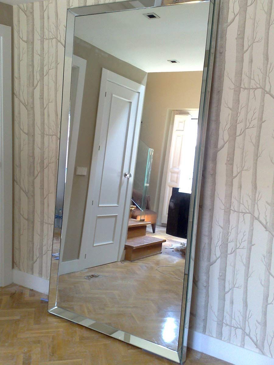 Espejo con iluminación LED, contra pared rayada, jarrón con césped a la izquierda, toma de corriente visible.