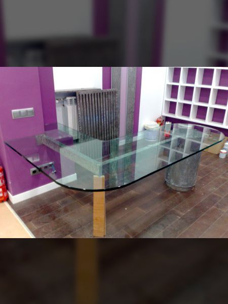 Mesa con tapa de cristal y patas de madera en una habitación con paredes moradas y suelo de madera oscura.
