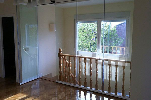 Paneles de vidrio cerca de una escalera con barandilla de madera y una vista de ventana soleada.