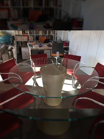 Mesa de vidrio ovalada con sillas rojas en una habitación con estanterías, un globo terráqueo y escritorios.