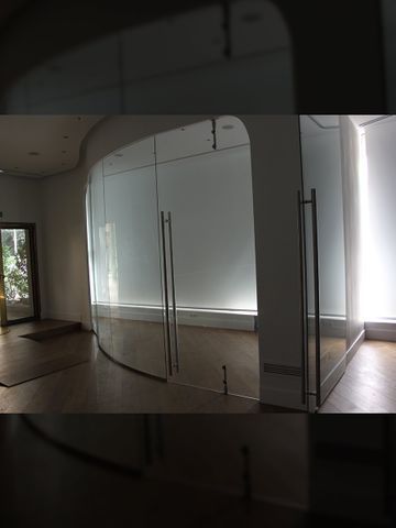 Habitación vacía con pared y puertas de vidrio curvo, piso de madera y paredes blancas.