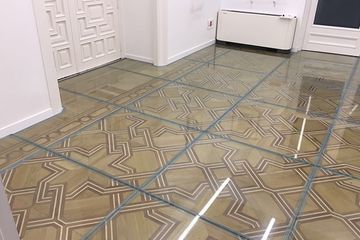 Azulejos de vidrio superpuestos a un piso de madera geométrico con una puerta y paredes blancas.