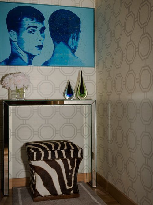 Obras de arte y decoración en un rincón: retratos azules, mesa con espejo, taburete con estampado de cebra y papel pintado geométrico.