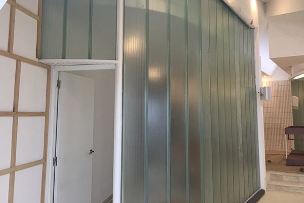 Una pared de bloques de vidrio curvados con una puerta y un marco blancos y paneles de pared blancos a la izquierda.