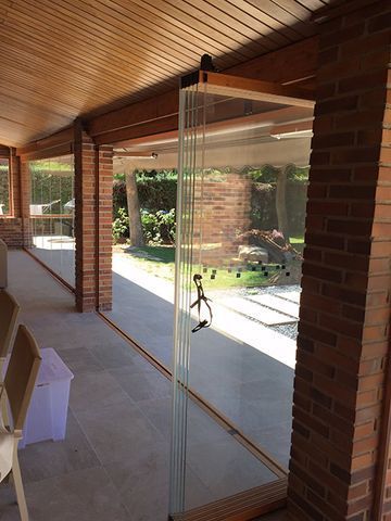 Puertas plegables de vidrio en un patio de ladrillo, abiertas a un patio soleado.