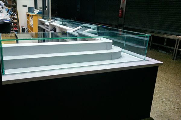 Un mostrador con gradas. Escalones blancos tras paneles de vidrio, sobre una base negra, en una tienda.