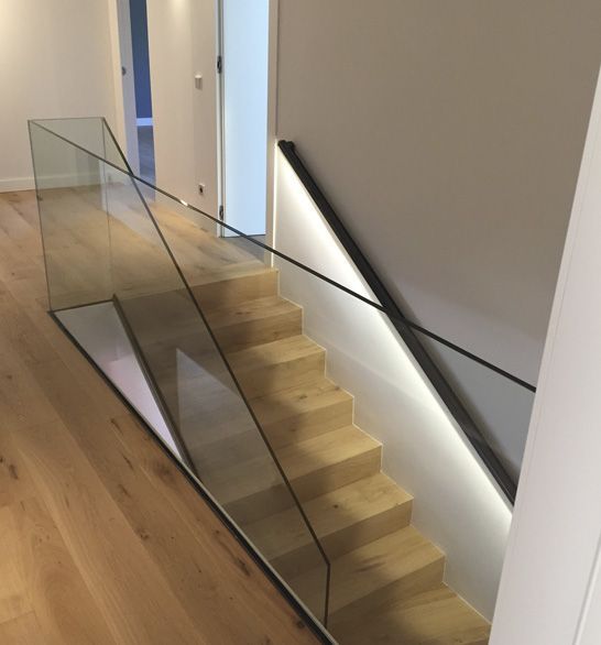 Escalera moderna con barandilla de cristal y escalones de madera, iluminada desde abajo.