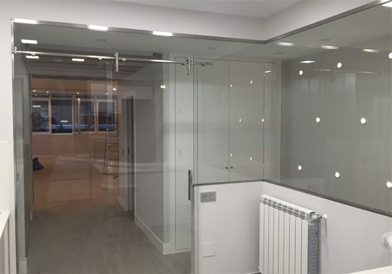 Entrada de oficina de cristal con paredes de cristal, techo iluminado y radiador.