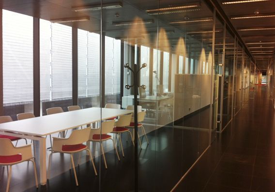 Pasillo de oficina moderno con sala de conferencias acristalada. Mesa y sillas blancas, suelo oscuro y perchero.