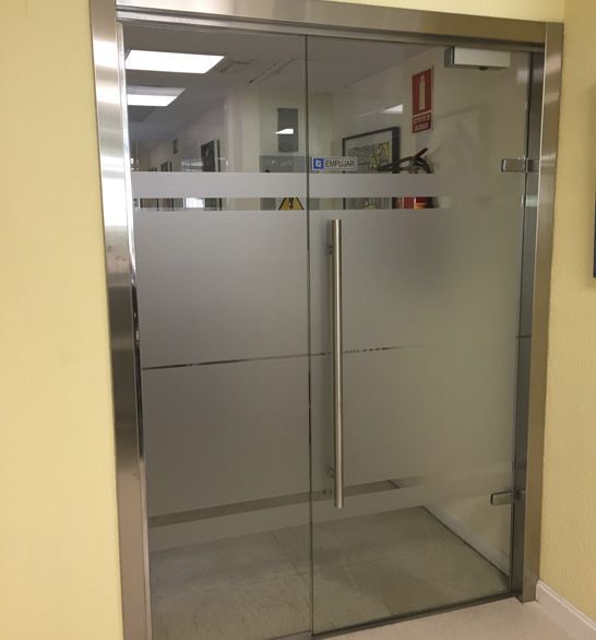 Puertas dobles de vidrio con franja horizontal esmerilada; marco de acero inoxidable.