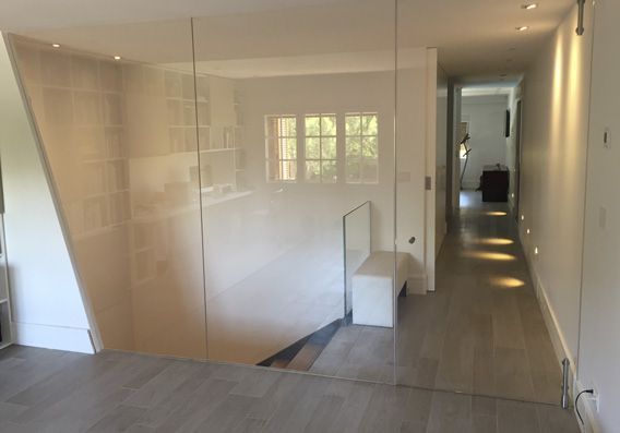 Escalera de cristal con paredes blancas, una ventana y un pasillo con suelo de madera e iluminación empotrada.