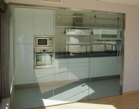 Cocina con puertas corredizas de vidrio, gabinetes blancos, electrodomésticos de acero inoxidable.