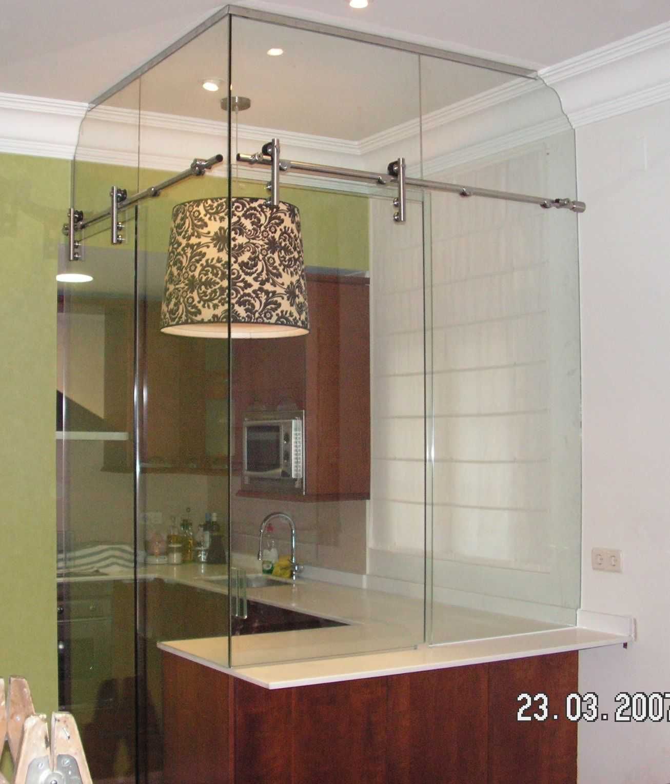 Barra de cocina cerrada con vidrio con luz colgante, gabinetes de madera y encimera blanca.