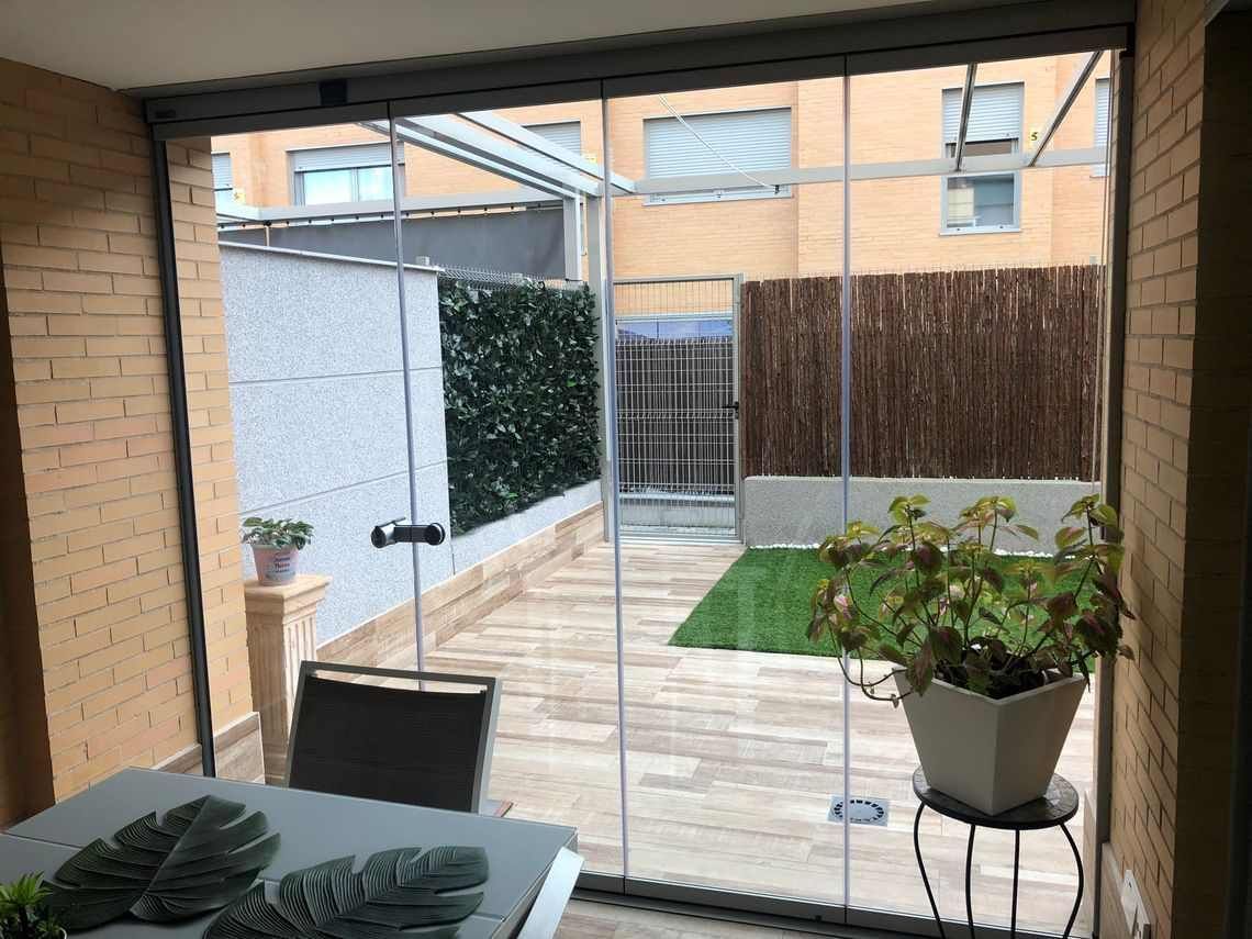 Las puertas de vidrio se abren a un patio al aire libre con plantas, que conduce a un patio trasero estrecho con una cerca de bambú.