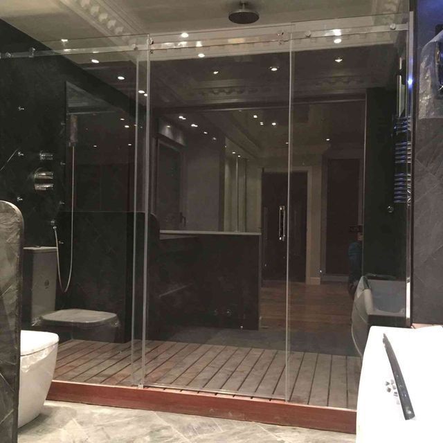 Mampara de ducha de cristal en un baño moderno con paredes oscuras y suelo de madera.