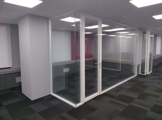 Oficina con paredes de cristal y marcos blancos. Suelo de moqueta, paredes grises y luces de techo.