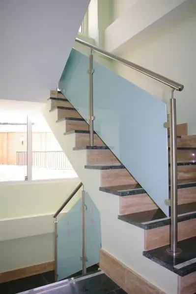 Escalera con paneles de vidrio y barandillas metálicas. Tonos beige y verde con luz natural.