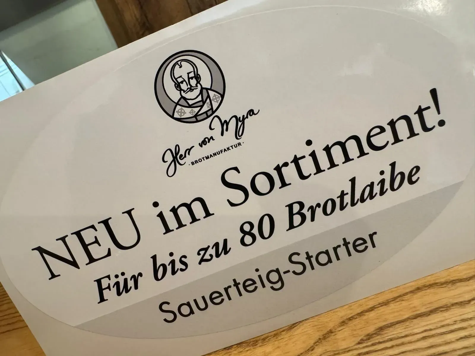 Schild mit dem Text: „NEU im Sortiment! Für bis zu 80 Brote, Sauerteigstarter“, darüber das Logo.
