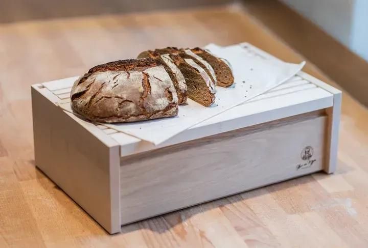 Brotlaib und Brotscheiben in einem hölzernen Brotkasten, drinnen.