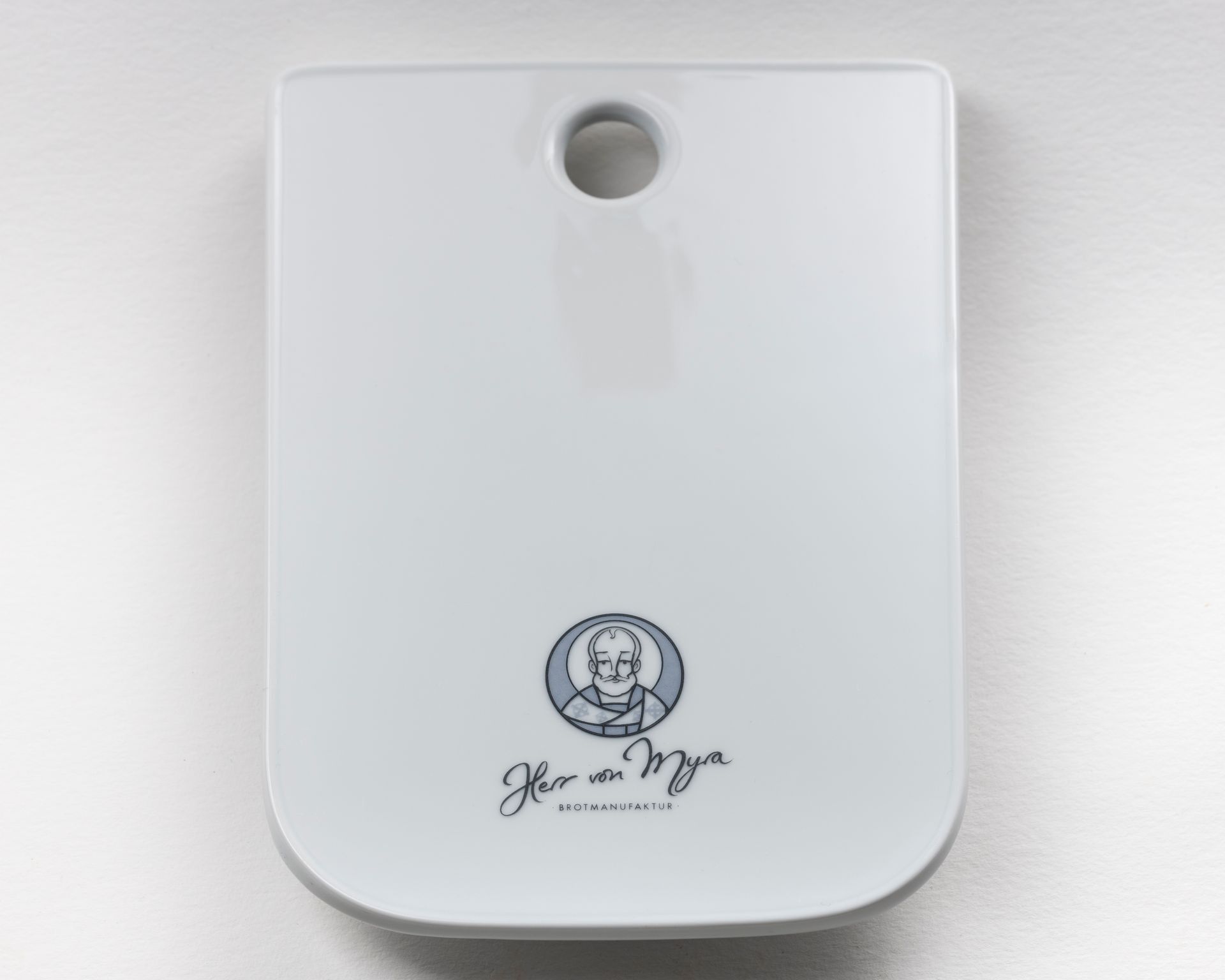 Weißes rechteckiges Schneidebrett mit einem Loch oben, unten mit einem Logo mit dem Porträt eines Mannes und Text.