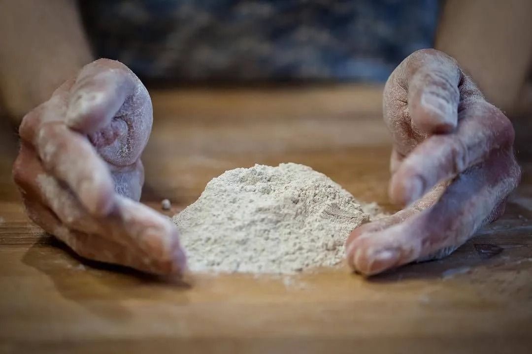 Hände formen auf einer Holzoberfläche einen kleinen Haufen Mehl, bereit zum Backen.