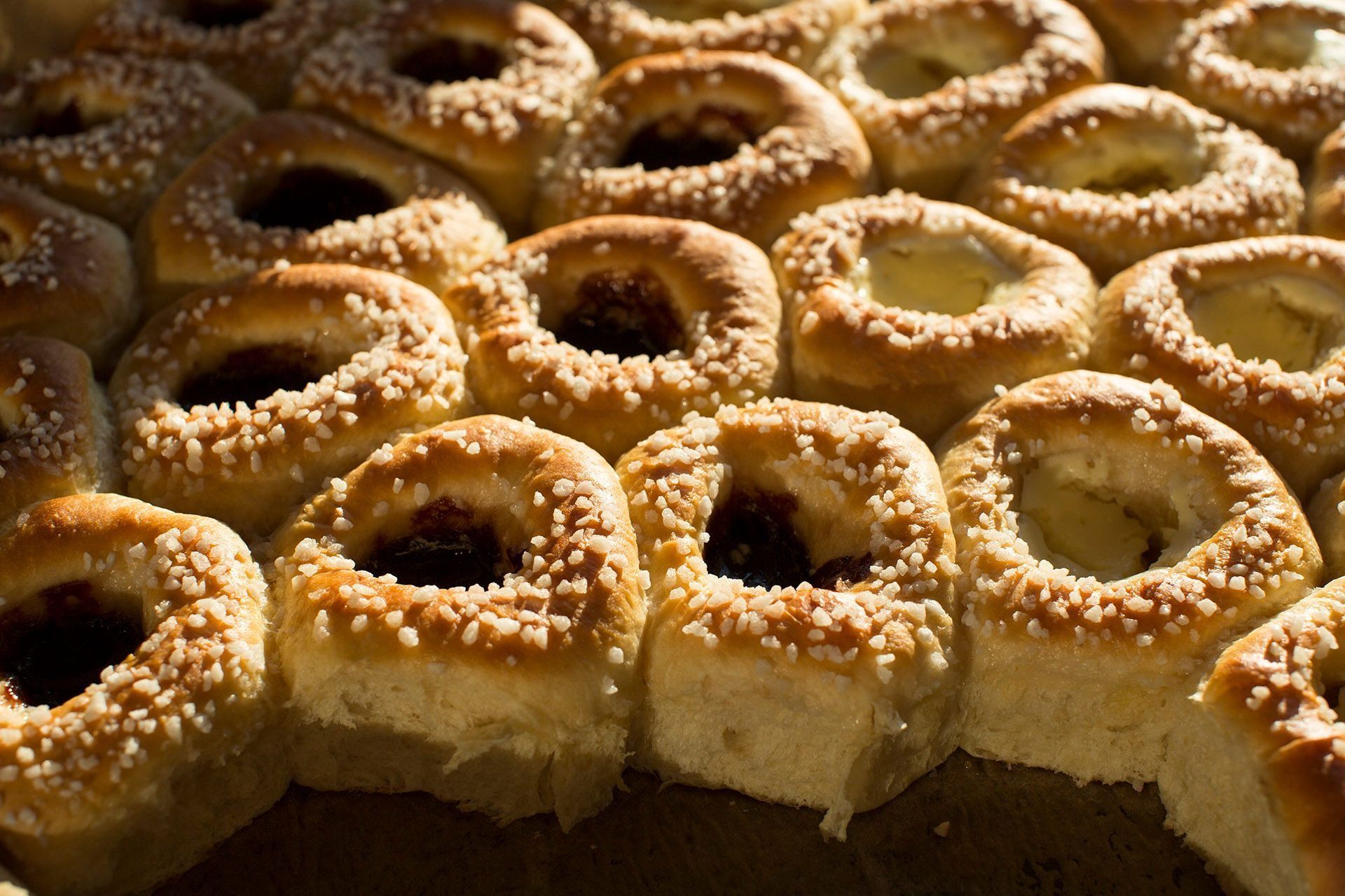 Nahaufnahme von goldbraun gebackenen Kolatschen, gefüllt mit Marmelade und Sahne und mit Zucker bestreut.