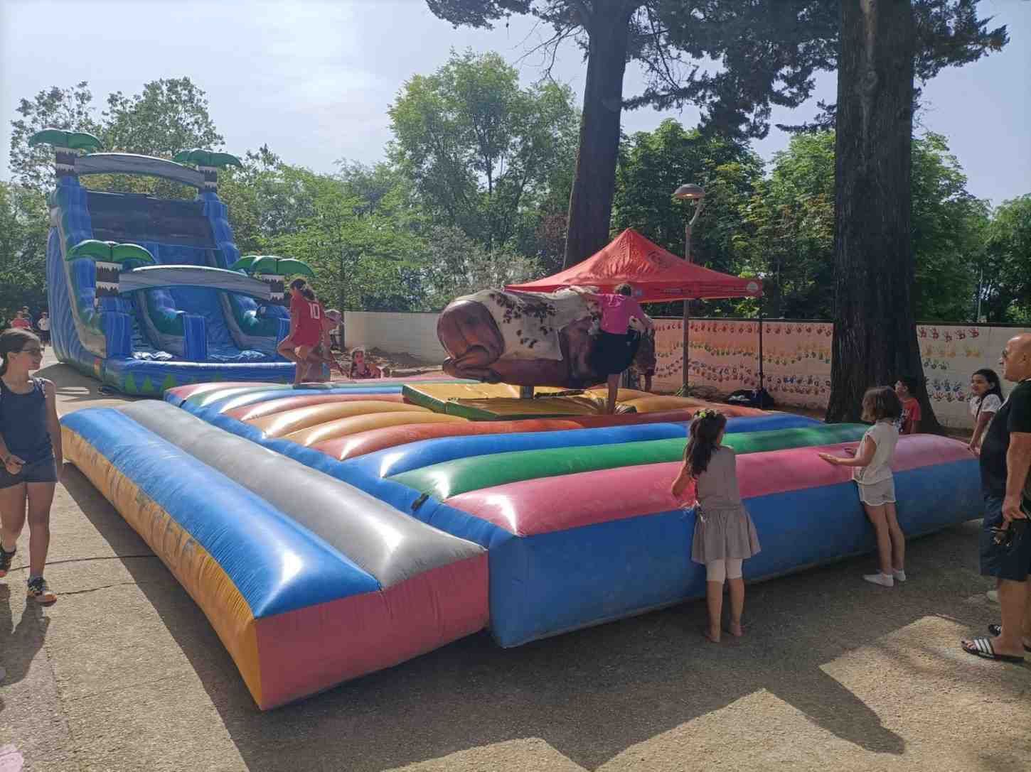 Tobogán hinchable y zona acolchada en un parque al aire libre, con niños de pie cerca.