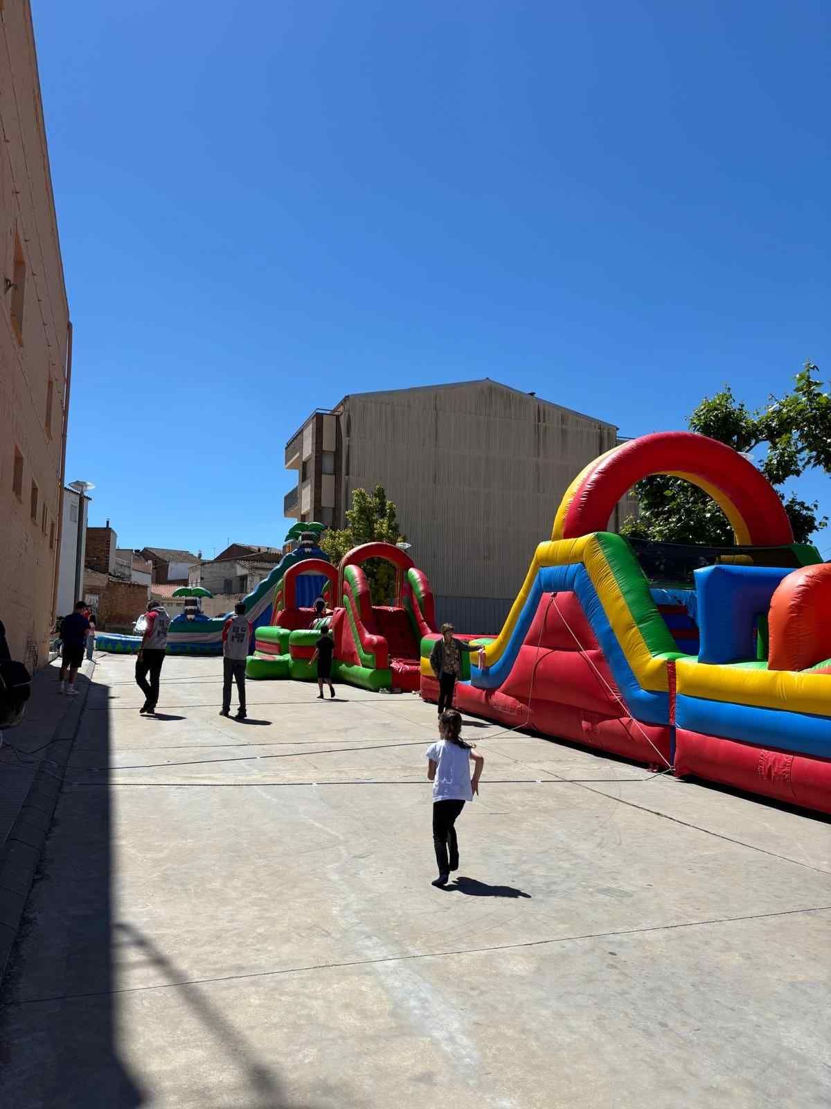 Parque hinchable al aire libre con coloridos toboganes y niños jugando en una calle soleada.