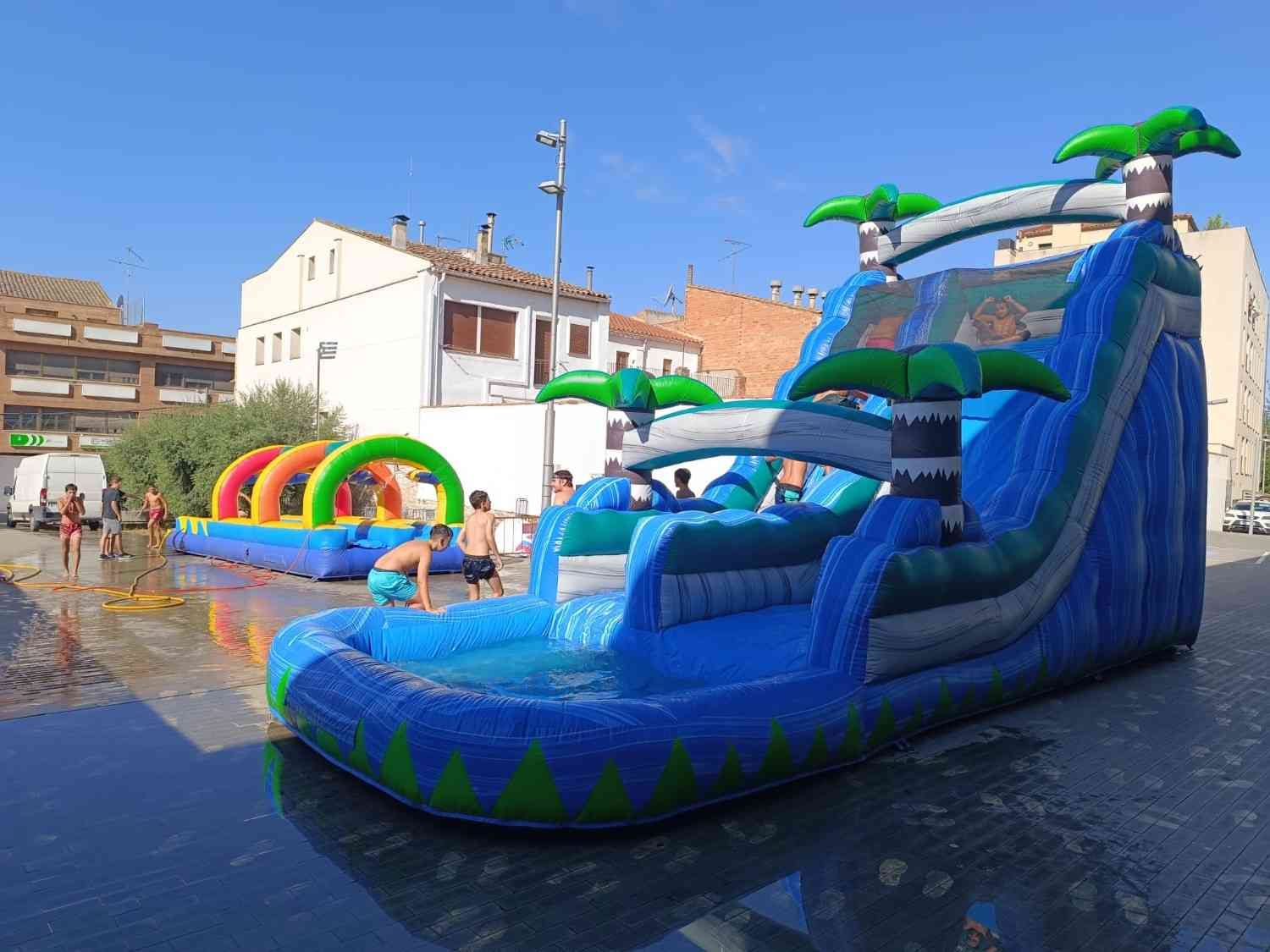 Tobogán acuático inflable azul en un parque acuático junto a la piscina, con arcoíris de fondo.