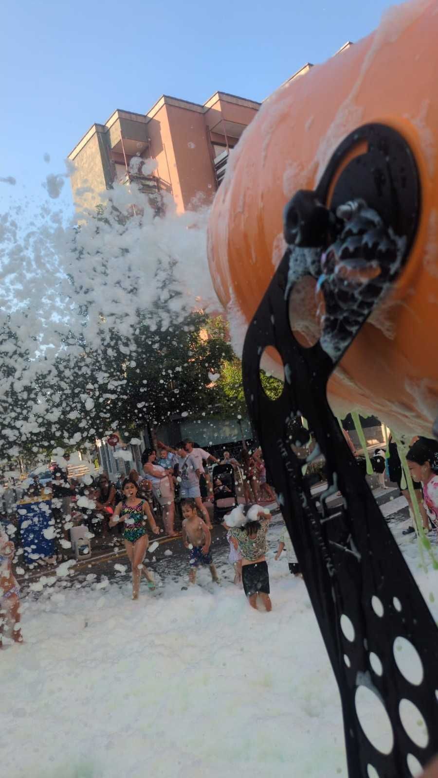 Un gran cañón de agua naranja rocía a una multitud en un evento en un parque acuático al aire libre.