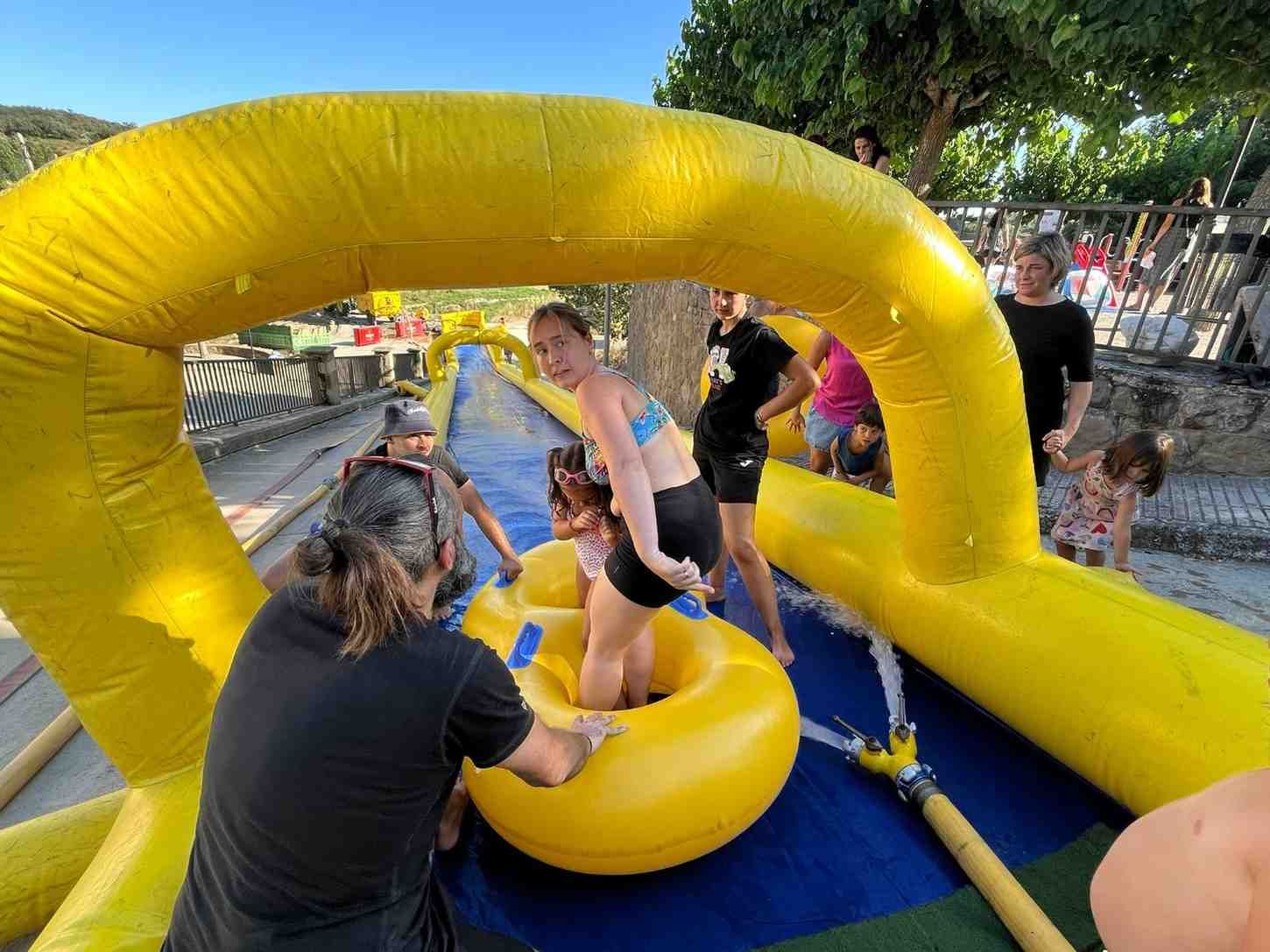 Personas montando en una pista de obstáculos inflable amarilla con salpicaduras de agua al aire libre.