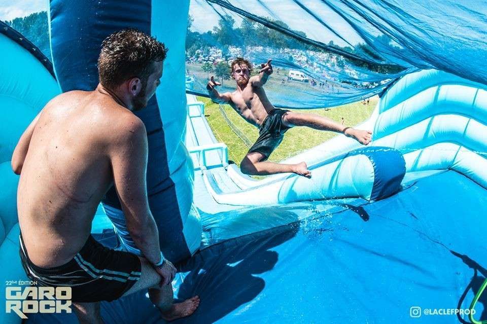 Dos personas en un tobogán acuático inflable azul, una sujetando el borde mientras la otra se desliza por el túnel.