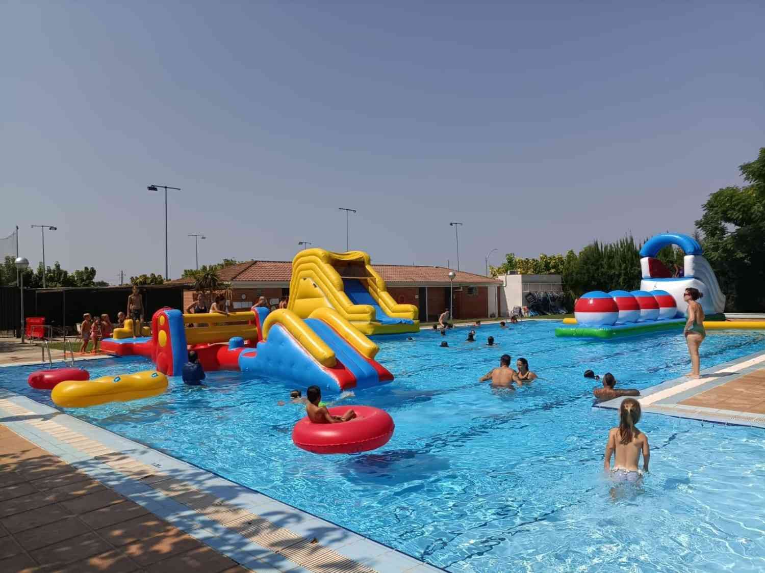 Gente nadando y jugando en una luminosa piscina al aire libre con coloridos toboganes e inflables.
