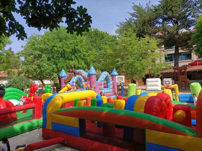 Parque hinchable colorido en un soleado parque infantil al aire libre con árboles y edificios al fondo.