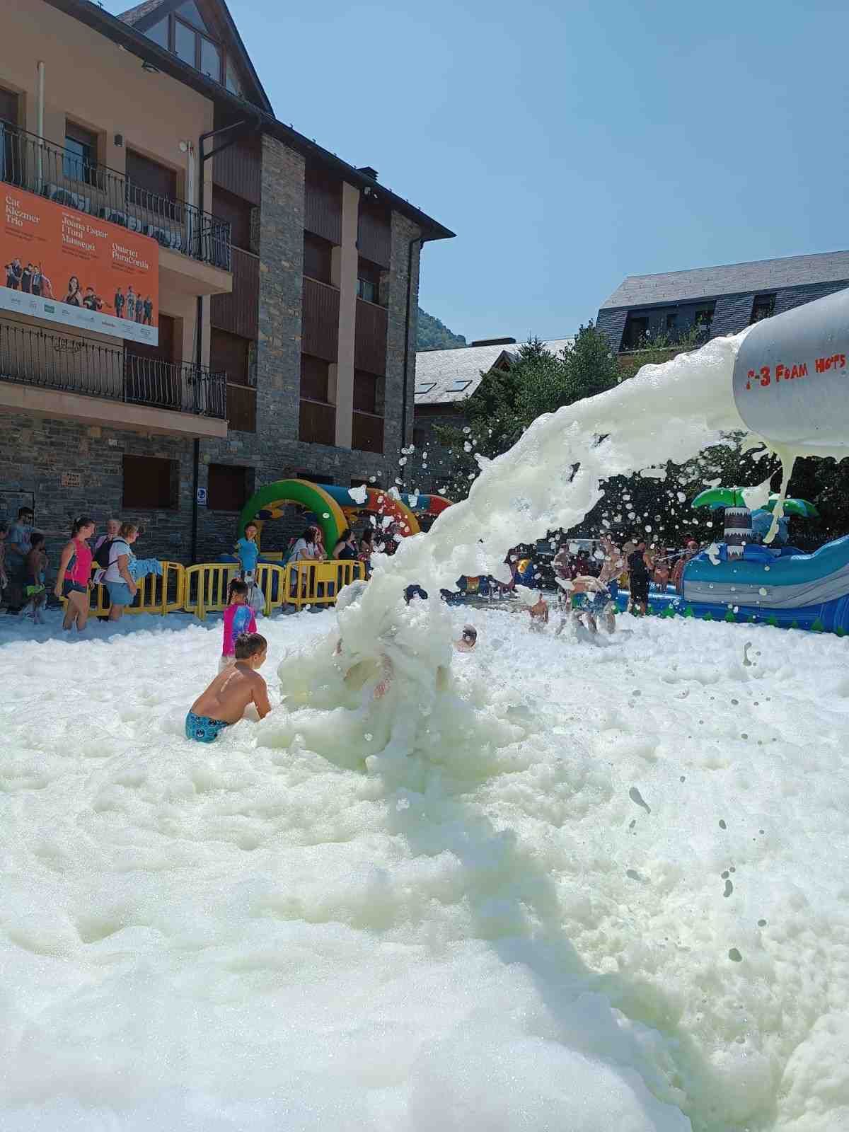 Tobogán acuático espumoso con gente chapoteando en una piscina exterior abarrotada junto a edificios.