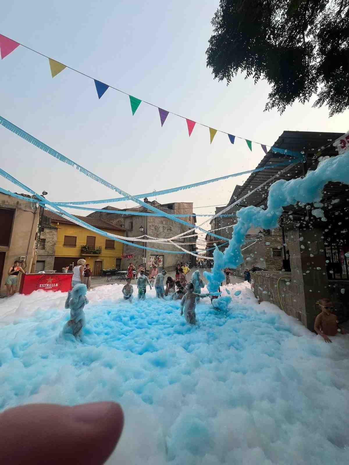 Niños jugando en un patio lleno de espuma azul, con guirnaldas de colores colgadas del techo.