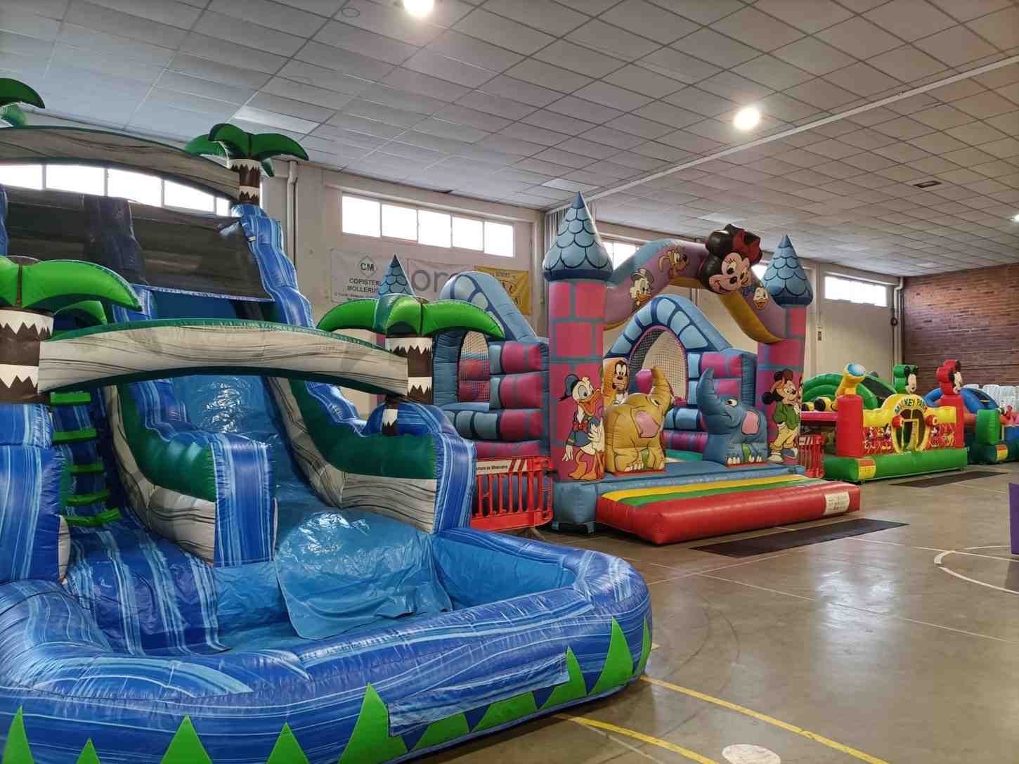 Zona de juegos hinchables cubierta con coloridas estructuras para saltar y toboganes en un amplio gimnasio.