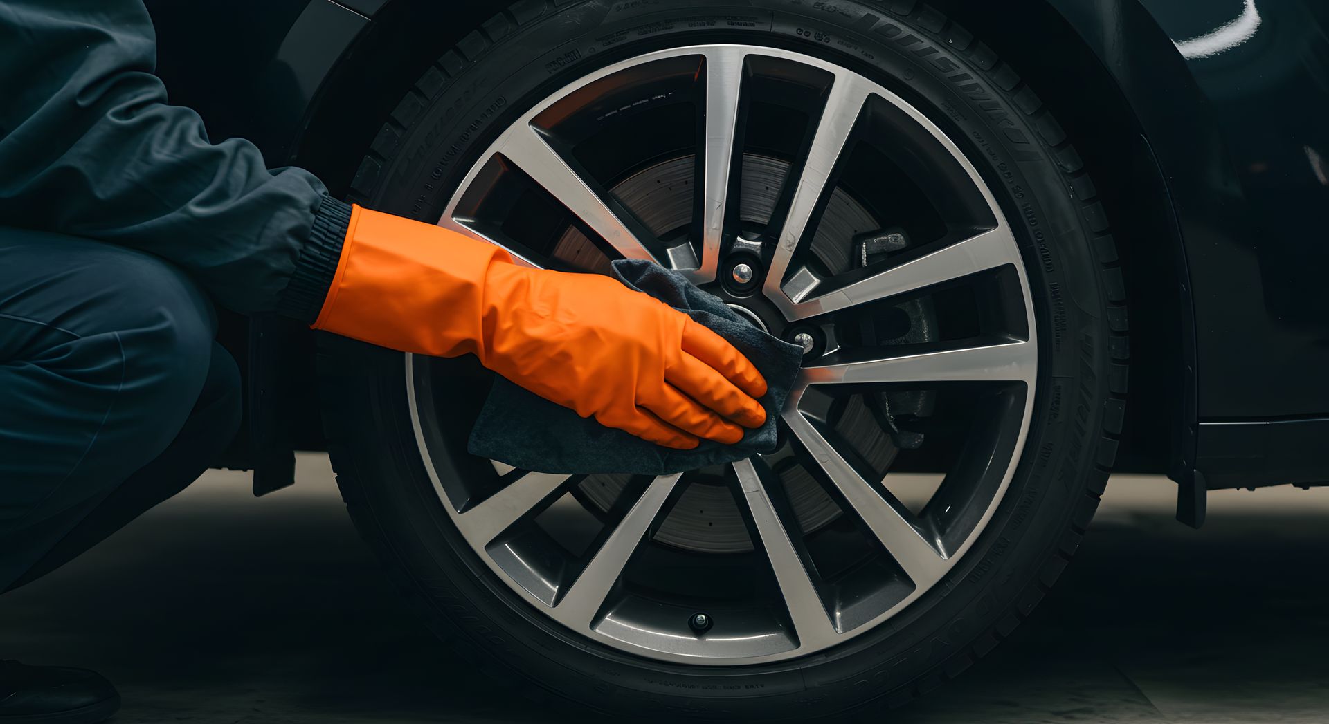 Une personne portant des gants orange nettoie une roue de voiture noire.