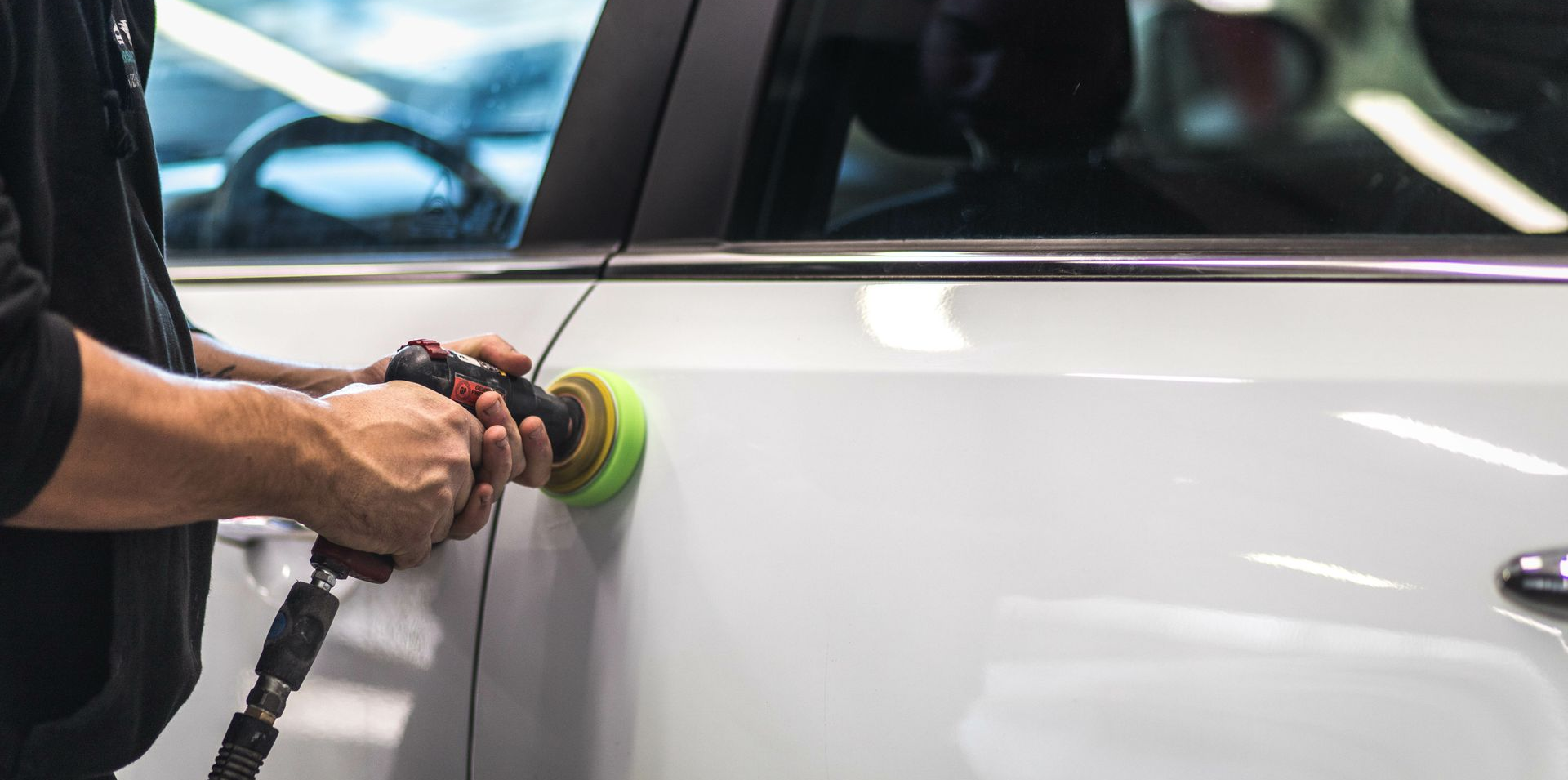 Une personne polissant une portière de voiture blanche avec une polisseuse orbitale.