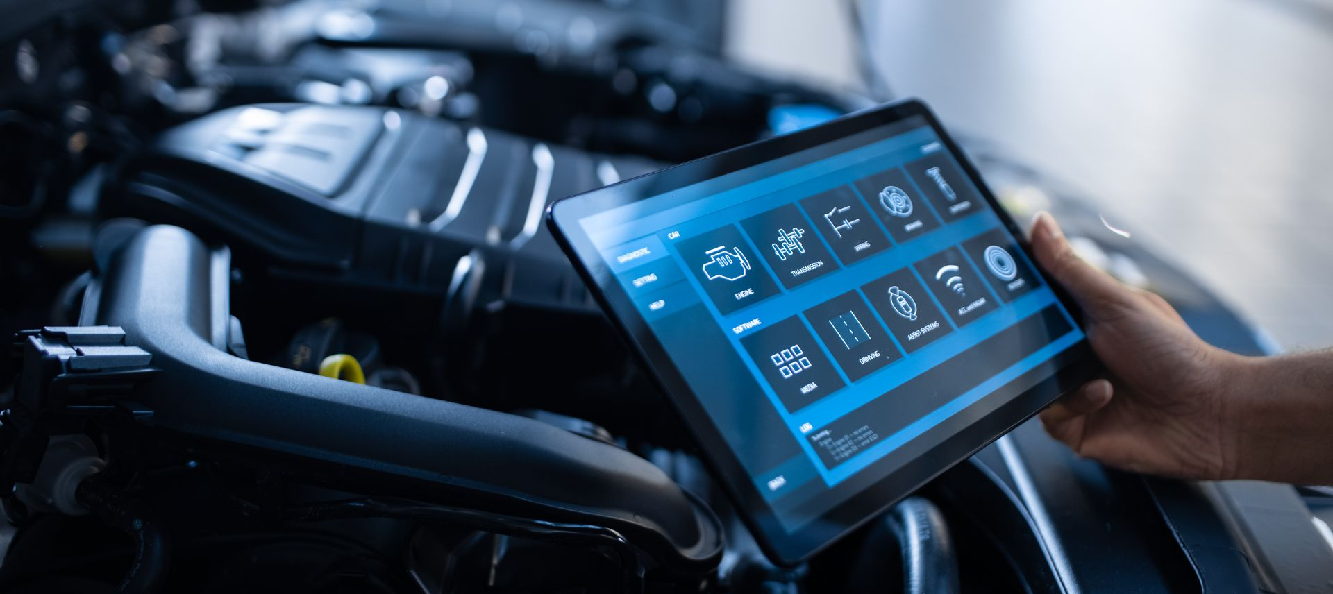 Une personne utilise une tablette pour diagnostiquer un moteur de voiture. La tablette affiche des informations de diagnostic.