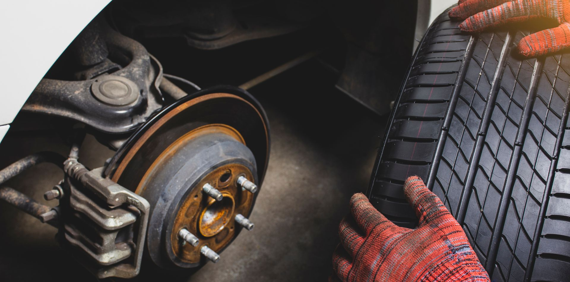 Un mécanicien ganté de rouge change un pneu. On aperçoit le disque de frein rouillé.