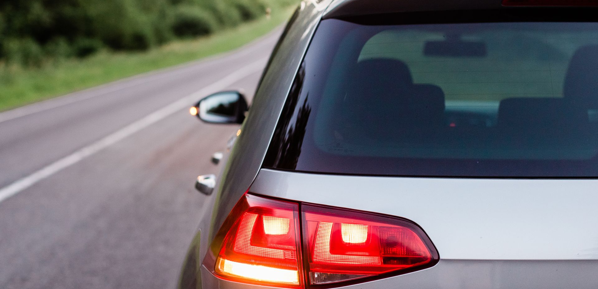 L'arrière d'une voiture argentée, feux stop allumés, roulant sur une route bordée de verdure.