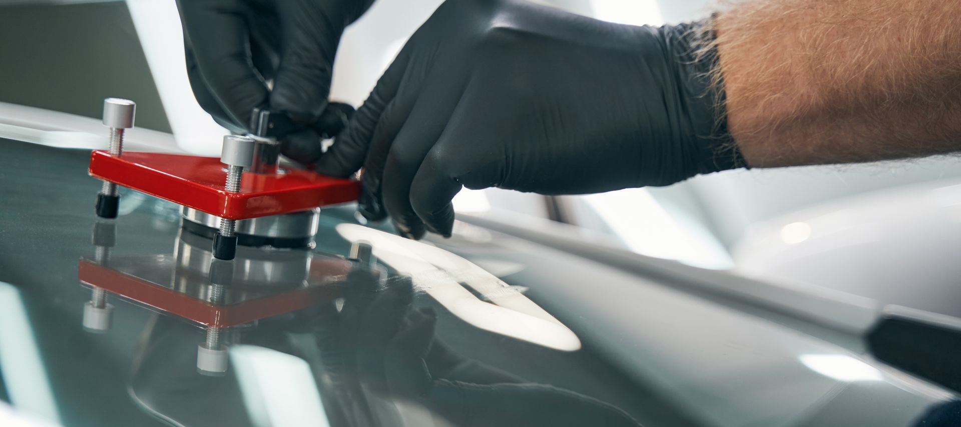 Une personne portant des gants noirs utilise un outil pour réparer une fissure dans un pare-brise de voiture.