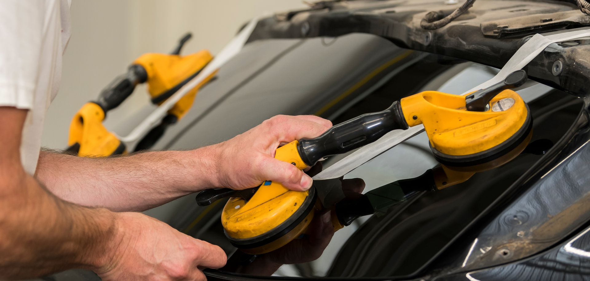 Une personne utilise des ventouses pour retirer un pare-brise d'un véhicule. Des outils jaunes et noirs sont visibles.